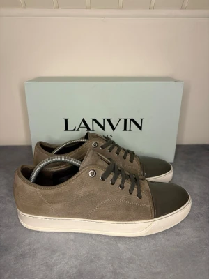 Lanvin sneakers grå, storlek 43-44 - Dessa lanvins ligger ute för försäljning. Dem är i fint skick men captoe är lite skadad. Sulkräm har använts för att fräscha upp skon. Endast box med följer! Dem är i storlek 43 men sitter som 44. Skickar inom 24h 🚀