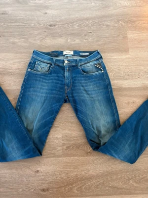 Blå jeans från Replay - Säljer ett par klassiska blå jeans från Replay Jeans med snygg tvätt och slitningar. Modellen har fem fickor, dragkedja och knappstängning samt kontrastsömmar. Tillverkade i bomull med en skön passform och läderpatch bak i midjan.