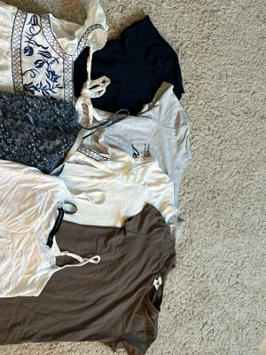 7 trendiga toppar i olika färger och stilar - Säljer ett paket med 7 snygga toppar i olika färger och modeller. Inkluderar svarta, vita, gråa och bruna toppar, både linnen och t-shirts.😍 Några har spetsdetaljer och knytband, en har blått broderi och en är paisleymönstrad. Perfekt för att mixa och matcha till olika outfits! 250kr för allt tillsammans💞
