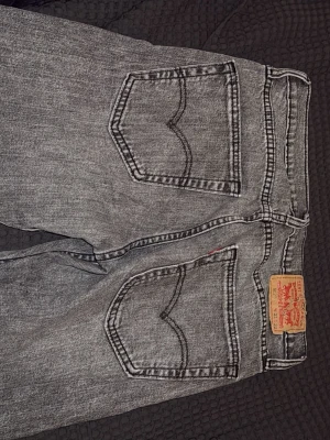 Grå Levi's 501 jeans - Säljer ett par grå Levi's 501 jeans med klassisk rak passform och fem fickor. Jeansen har en vintage tvätt och tydliga sömmar på bakfickorna. Tillverkade i bomull och har knappgylf. Perfekta för en avslappnad och stilren look.