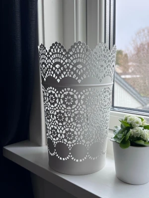 Vit spetsmönstrad metallkruka - Säljer en vit kruka i metall med detaljerat spetsmönster och vågig kant. Perfekt som blomkruka eller förvaring av småsaker. Ger ett stilrent intryck i rummet.