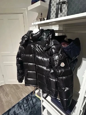 Svart glansig dunjacka från Moncler - Säljer nu min moncler jacka som i nypris kostar upp mot 16,000kr om inte mer. Den har ett litet hål under fickan men som inte syns alls mycket, säljer då sommaren närmar sig men är en helt perfekt vinterjacka. Köptes hösten 2025 