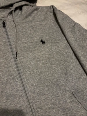 Ralph Lauren zip | Strl M - Snygg och tidlös zip hoodie från Polo Ralph Lauren i klassisk grå färg. 🤩 Mörkblå broderad logga på bröstet.  ✅Storlek M, och är i mycket fint skick ✅Perfekt basic som funkar året runt. Hör av er vid några frågor så löser vi de🤩