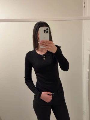 Svart topp - En svart, ribbad långärmad topp med rund halsringning. Toppen har en slim passform och är tillverkad i ett mjukt och stretchigt material som sitter snyggt på kroppen. Perfekt att styla med jeans eller kjol för en clean look. Från h&m.