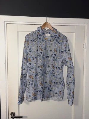 Blommig skjorta från Ben Sherman Riley - Snygg slim fit skjorta från Ben Sherman Riley i ljusblått med blommigt och fågelmönster. Skjortan har långa ärmar, klassisk krage och knäppning framtill. Perfekt för dig som vill sticka ut med ett färgglatt och unikt plagg.