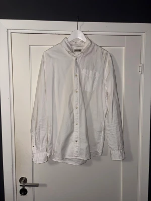 Vit skjorta från Jack & Jones - Klassisk vit skjorta från Jack & Jones med lång ärm och bröstficka. Skjortan har knäppning framtill och är gjord i ett mjukt bomullstyg. Perfekt till både jeans och chinos för en clean look.