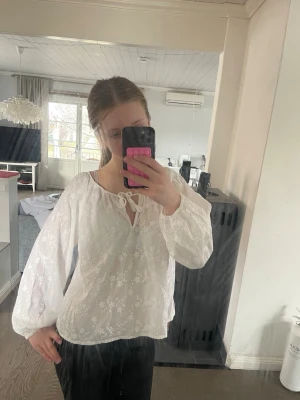 Vit blommig blus med knytning - Söt vit blus med diskret blommönster och luftig passform. Blusen har långärmade ballongärmar och en rundad halsringning med knytband framtill. Endast använd en gång. Den är i Stolek XS men skulle säga att den passar bättre som S💕