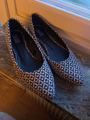 Svarta och vita ballerinaskor Camaieu - Säljer ett par ballerinaskor från Camaieu med spetsig tå. Skorna har ett svart och vitt grafiskt mönster och är tillverkade i textilmaterial. Perfekta för dig som gillar stilrena men ändå unika skor med snygg design.