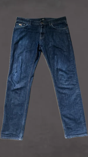 Blå raka jeans från BOSS - Snygga blå jeans från BOSS med rak passform och klassisk femficksdesign. Jeansen har normal midja, och är gjorda i ett slitstarkt denimtyg. Perfekta för en avslappnad och stilren look.