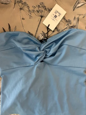Ljusblå bandeau topp från Bik Bok - Trendig ljusblå bandeau topp från Bik Bok med snygg twistdetalj framtill. Toppen är axelbandslös och croppad, perfekt för en modern och stilren look. Tillverkad i mjukt material som känns skönt mot huden.💙