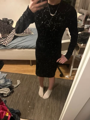 Svart glittrig sammetsklänning - Snygg svart klänning i sammet med glittriga detaljer. Figurnära modell med lång ärm och rund halsringning. Perfekt för dig som vill sticka ut lite extra med ett coolt stjärnmönster och skön känsla.