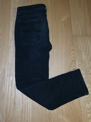 Mörkblå/ svarta slim jeans från Nudie Jeans - Säljer ett par mörkblå/svarta slim jeans från Nudie Jeans med klassisk femficksdesign och knappgylf. Jeansen har en smal passform och är tillverkade i slitstark denim. Perfekta för dig som gillar en stilren och enkel look. Passar perfekt på 163cm. Ett hål som är sytt i affär som syns på sista bilden. Utöver det i fint skick. Hör gärna av er vid frågor👍