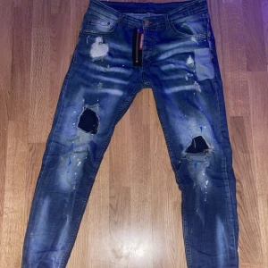 Dsquared2 Jeans storlek 32/M - Snygga blå jeans från Dsquared2 med slitna detaljer och hål för en trendig look. De har en dragkedja och knapp framtill samt klassiska fem fickor. Perfekta för en avslappnad stil.