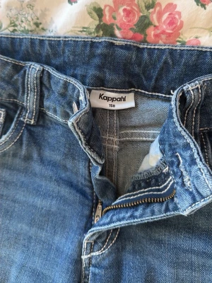 Blå bootcut jeans från Kappahl - Snygga blå bootcut jeans från Kappahl i storlek 158. Jeansen har klassisk femficksdesign, dragkedjegylf och vita kontrastsömmar. Tillverkade i mjukt denimtyg som ger en avslappnad look. Perfekta till en trendig vardagssti.