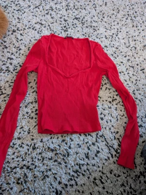 Röd ribbad långärmad topp stl xxs - Trendig röd ribbad topp med lång ärm och snygg v-ringad halsringning. Figurnära passform och stretchigt material som sitter skönt. Perfekt att styla med jeans eller kjol för en cool look.