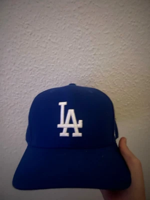 Blå LA keps snapback - Snygg blå keps med LA-logga broderad i vitt framtill. Klassisk snapback-modell med justerbar plastrem bak. Perfekt accessoar för en sportig och avslappnad stil. Knappt använd. Kan gå ner i pris vid snabb affär