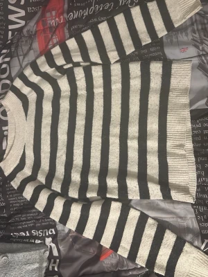 Randig stickad tröja i svart och vitt - Säljer en stickad tröja med breda svarta och vita ränder. Tröjan har rund hals, långa ärmar och ribbstickade muddar vid hals, ärmslut och nederkant. Perfekt för dig som gillar klassiska mönster och enkel stil.