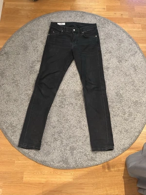 Svarta skinny jeans från J.Lindeberg - Snygga svarta skinny jeans från J.Lindeberg med klassisk femficksmodell och silverfärgade detaljer. Jeansen har en smal passform och är tillverkade i ett stretchigt bomullsmaterial för extra komfort. Perfekta för en stilren och modern look.