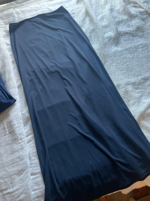 Mörkblå långkjol i mjukt tyg - En stilren mörkblå långkjol med rak passform. Kjolen är enkel och utan detaljer, vilket gör den lätt att matcha med olika toppar. Tillverkad i ett mjukt och följsamt material som ger en snygg siluett.