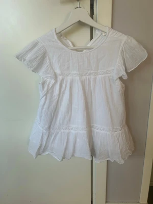 Vit volangblus med spetsdetaljer💕💕 - Säljer en vit blus med volangkant och spetsdetaljer💕💕Blusen har korta ärmar, rund halsringning fram och v-ringning bak💕💕 Tillverkad i ett lätt, luftigt bomullstyg som ger en flowy känsla💕💕I bra skick💕💕Jag säljer den för 50 kr💕💕Hör av er vid en intresse💕💕💕