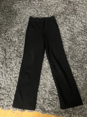 Svarta kostymbyxor med raka ben - Snygga svarta kostymbyxor med raka ben och hög midja. Klassisk design med fickor fram och hällor för skärp. Perfekta till en stilren look och passar till många olika outfits.