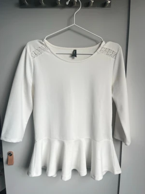 Vit topp med volang och spetsdetalj - Säljer en vit topp från H&M med volang nedtill och fina spetsdetaljer på axlarna. Toppen har trekvartsärm och rund halsringning. Perfekt för dig som gillar en feminin och enkel stil. Storleken säger XL men den passar som en S. Hör av dig innan köp!🤗