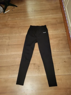 Svarta leggings från SOC - Säljer ett par svarta leggings från SOC med diskret logga på höften. De har hög midja och smal passform som sitter tight längs benen. Perfekta till träning eller chill. Materialet känns stretchigt och bekvämt.