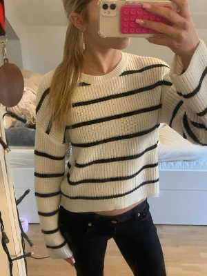 Vit stickad tröja med svarta ränder - Säljer en vit stickad tröja med svarta horisontella ränder. Tröjan har rund halsringning, långa ärmar och en något kortare passform. Perfekt för dig som gillar en enkel och stilren look. Materialet är grovt stickat och känns mjukt mot huden. Storlek 146/152 men passar mig som bär XS bara lite kort i armarna. Använd en gång