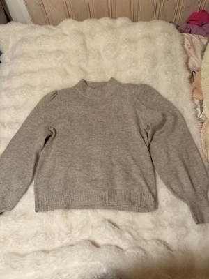 Beige stickad tröja från JDY - Mysig beige stickad tröja från JDY med rund halsringning och ribbade muddar vid ärmslut och nederkant. Tröjan har en enkel och stilren design som passar perfekt till höst och vinter. Materialet känns mjukt och bekvämt.