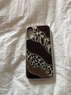 Mobilskal med djurmönster och metallic - Snyggt mobilskal med olika djurmönster i svart, brunt, beige och vitt. Skalet har en glansig finish och inslag av metallicdetaljer. Passar perfekt för dig som vill ha ett unikt och trendigt skydd till mobilen. Tillverkat i hårdplast.