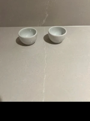 Två små vita äggkoppar - Säljer två små runda äggkoppar i vitt porslin. Enkel och stilren design som passar in i de flesta kök. Skålarna är släta och blanka med en klassisk form.