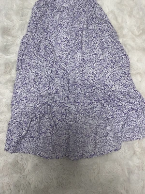  blommig kjol med en rosett vid sidan  - Söt kjol med blommigt mönster i lila och vitt. Kjolen har volangdetaljer och är gjord i ett lätt och luftigt material, perfekt för varmare dagar. Står att det är st11-12 men är mer till 9-10!