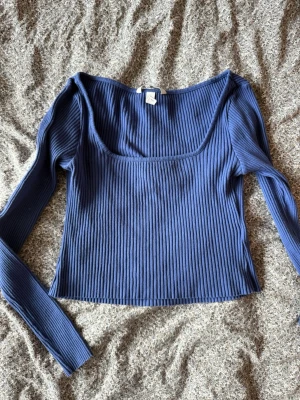 Blå ribbad långärmad topp H&M - Säljer en blå ribbad långärmad topp från H&M. Toppen har en croppad passform och bred, fyrkantig urringning. Perfekt att styla med höga jeans eller kjol för en trendig look.