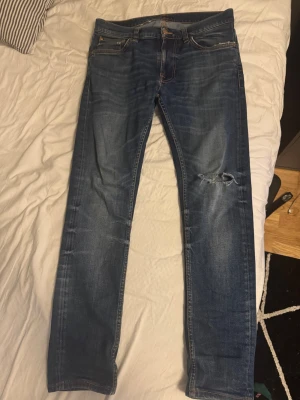 Blå nudie jeans! - Tja! Säljer ett par blå jeans från Nudie Jeans med slim fit och klassisk femficksmodell. Jeansen har slitningar och ett hål på ena benet för schysst detalj. Tillverkade i denim med snygga tvättade detaljer och kontrastsömmar. Ny pris är cirka 1500 men mitt pris endast 699kr. Inte hugget i sten så hör av er vid minsta lilla fråga 😻