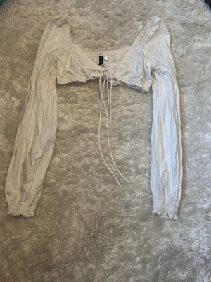 Vit croppad blus med snörning - Supersöt vit croppad blus från H&M med långa puffärmar och snörning framtill. Blusen har en fyrkantig ringning och elastiska muddar vid ärmsluten. 