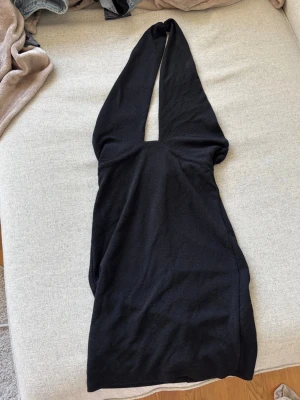Svart kort klänning med djup v-ringning - Säljer en svart kort klänning med djup v-ringning och halterneck. Klänningen har en tight passform och är ärmlös, perfekt för dig som vill ha en stilren och enkel look. Materialet känns mjukt och stretchigt. Dragkedja bak. Från BikBok i storlek S.