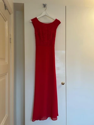 Röd långklänning från Esprit i storlek 34 - Elegant röd långklänning med rund halsringning och vackert broderat liv. Klänningen har ett flytande, lätt tyg och ett dekorativt knytband i midjan baktill. Perfekt för speciella tillfällen såsom bal!