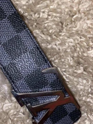  damierbälte - Snyggt bälte i svart och grått damiermönster. Bältet har ett metall och är gjort i ett tåligt konstlädermaterial. Perfekt accessoar för att lyfta din outfit med en lyxig touch.