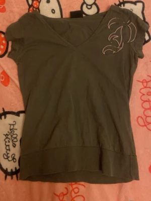 Vintage grön v-ringad topp Peak Performance - Snygg grön vintage v-ringad topp från Peak Performance med korta ärmar och broderad detalj vid axeln. Tillverkad i mjuk bomull som känns skön mot huden. Perfekt till jeans eller kjol för en avslappnad look.