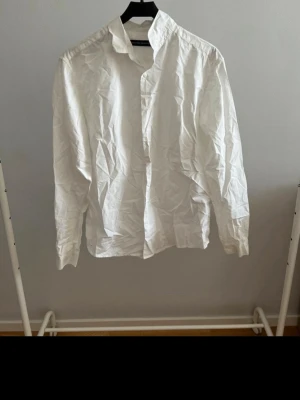 Klassisk vit skjorta i bomull - Säljer en klassisk vit skjorta med lång ärm och knappar framtill. Skjortan har en tidlös design med krage och är tillverkad i bomull, vilket gör den både bekväm och enkel att styla. Perfekt basplagg för garderoben!