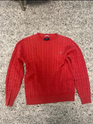 Röd kabelstickad tröja från Gant - Säljer en röd kabelstickad tröja från Gant med rund halsringning och diskret logga broderad på bröstet. Tröjan har ribbade muddar vid ärmslut och nederkant. Perfekt för dig som gillar klassisk och stilren design.     Pris kan diskuteras 