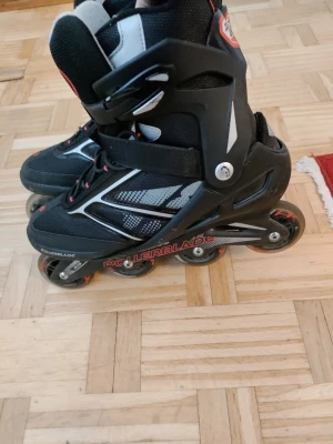 Svarta inlines Rollerblade Zetrablade - Säljer ett par svarta inlines från Rollerblade, modell Zetrablade. De har detaljer i rött, vitt och grått samt justerbart spänne och kardborreband för bra passform. Hårda plastskal och ventilerande meshpartier gör dem perfekta för träning och fritid.
