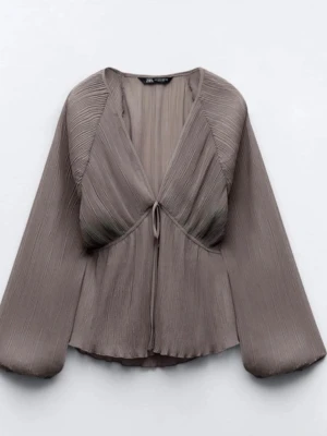 Plisserad brun blus från Zara - Trendig brun plisserad blus från Zara med djup V-ringning och knytning framtill. Blusen har vida, långa ärmar och är tillverkad i ett lätt, transparent material som ger ett luftigt intryck. Perfekt för dig som gillar en avslappnad men stilren look.