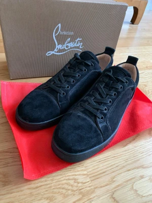 Svarta mockasneakers Christian Louboutin - Snygga svarta sneakers från Christian Louboutin i mjuk mocka med matchande svarta skosnören och diskret logga på hälen. Låg modell med klassisk siluett och svart yttersula. Perfekta för dig som gillar stilrena och exklusiva skor.