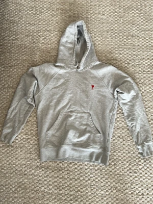 Grå hoodie från Ami Paris - Snygg grå hoodie från Ami Paris. På bröstet finns Ami Paris ikoniska röda hjärta med A-broderi. Tillverkad i mjuk bomullsblandning som är perfekt för en avslappnad stil. Storlek s-m