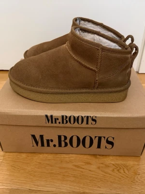 Bruna stövletter från Mr.BOOTS - Säljer ett par bruna stövletter från Mr.BOOTS i mocka med mjukt, luddigt foder på insidan. Skorna har en rund tå, låg ankelhöjd och grov sula i gummi. Perfekta för kalla dagar och riktigt sköna att ha på sig.