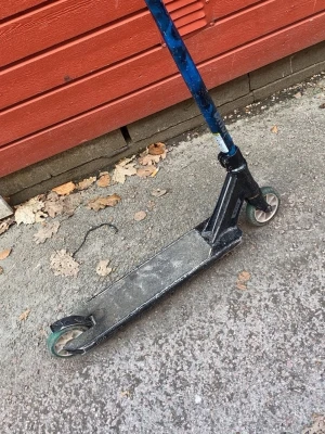Svart trick sparkcykel med blått styre - Säljer en svart trick sparkcykel från District med blått styre och gröna hjul. Styret har ett coolt mönster i blått och svart. Perfekt för dig som gillar att köra i skateparken eller bara vill cruisa runt. Tillverkad i metall för extra hållbarhet.