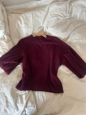 Vinröd stickad tröja med vida ärmar - Mysig vinröd stickad tröja med breda, trekvarts långa ärmar och ribbade muddar vid ärmslut och nederkant. Tröjan har en rak passform och rund halsringning. Perfekt för lager på lager och höstmys.