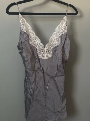 Grått linne med spets från Zara - Snyggt grått linne från Zara med tunna axelband och v-ringning dekorerad med vit spets. Tillverkat i ett glansigt, mjukt material som känns lyxigt mot huden. Perfekt för mysiga kvällar hemma. (Skrynkligt från garderoben, inget fel på det men har för mycket kläder så rensar nu) 💕💕🥲💪🏼