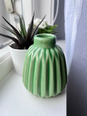 Grön keramikvas med räfflat mönster - Säljer en liten grön vas i keramik med räfflat mönster och blank yta. Perfekt för enstaka blommor eller som dekoration. Färgen är ljusgrön och den har fått små sprickor i materialet.
